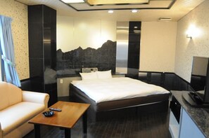 A modern hotel room with a bed, a sofa, a small table, and a TV. - Business Inn Nagashima (Kisosaki)