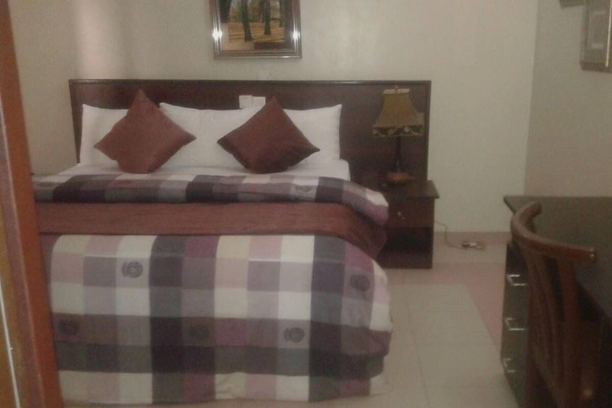 Quarto com cama, mesa de cabeceira, abajur e escrivaninha.