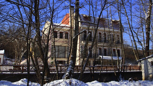 A two-story building with a red roof, surrounded by snow-covered trees and a wooden fence. - Butterfly Butik Hotel (Kirklareli)