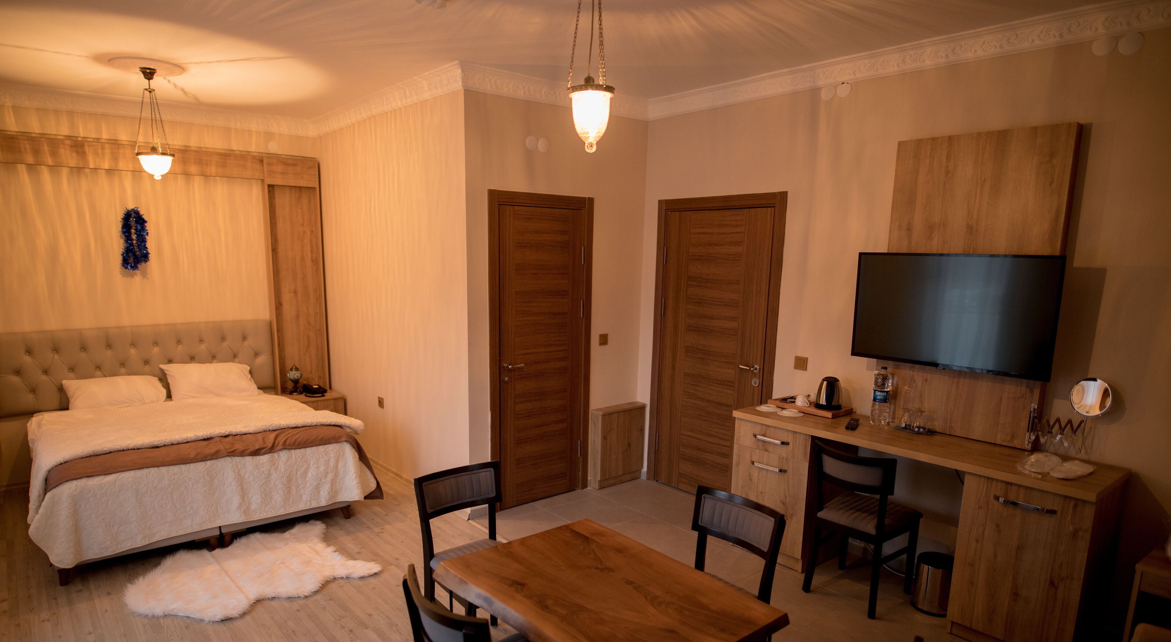 A hotel room with a large bed, a wooden desk, a television, and a small table.