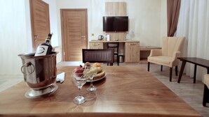 A hotel room with a wooden dining table, a TV mounted on the wall, a minibar, and a seating area with a chair. - Butterfly Butik Hotel (Kirklareli)