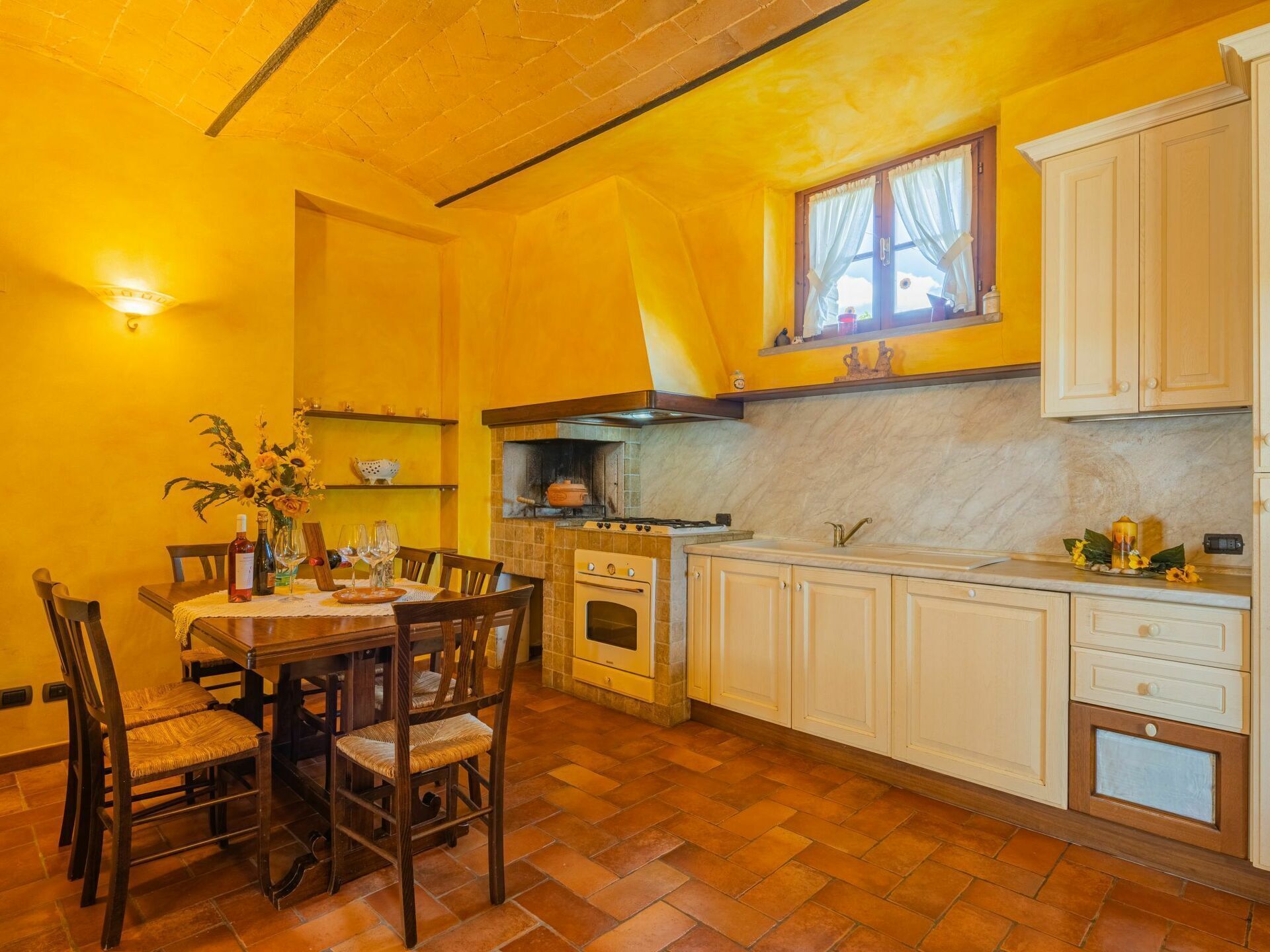 A kitchen with a brick floor, wooden table, and chairs, a stove, oven, and white cabinets.