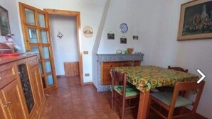 A dining area with a wooden table and chairs, a kitchen area with a stove and cabinets, and a door leading to another room. - Apartment 117 M² in a beautiful condominium house  (Arzachena)