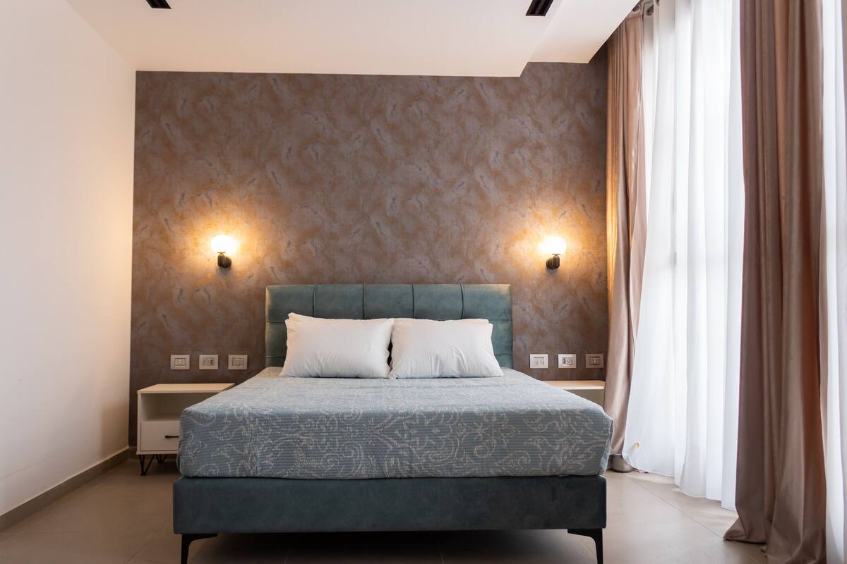 A modern bedroom with a large bed, two wall-mounted lights, and a nightstand.