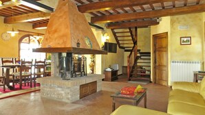 Un interno rustico con travi in legno a vista, un camino in pietra, una zona pranzo con sedie di legno e una scala.