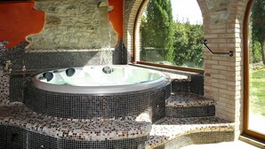 Una vasca idromassaggio con sedute in mosaico, una parete in pietra e vista attraverso una finestra.
