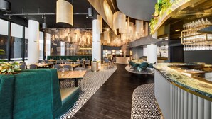 A modern restaurant interior with high ceilings, pendant lighting, and a bar area.