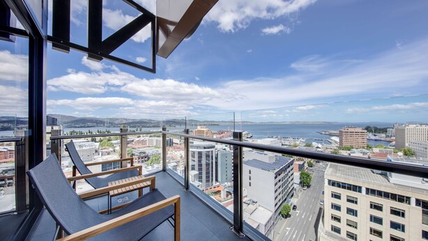 A balcony with two lounge chairs and a city view.