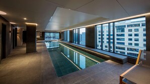 A modern hotel corridor with a glass pool, large windows, and a view of the cityscape.