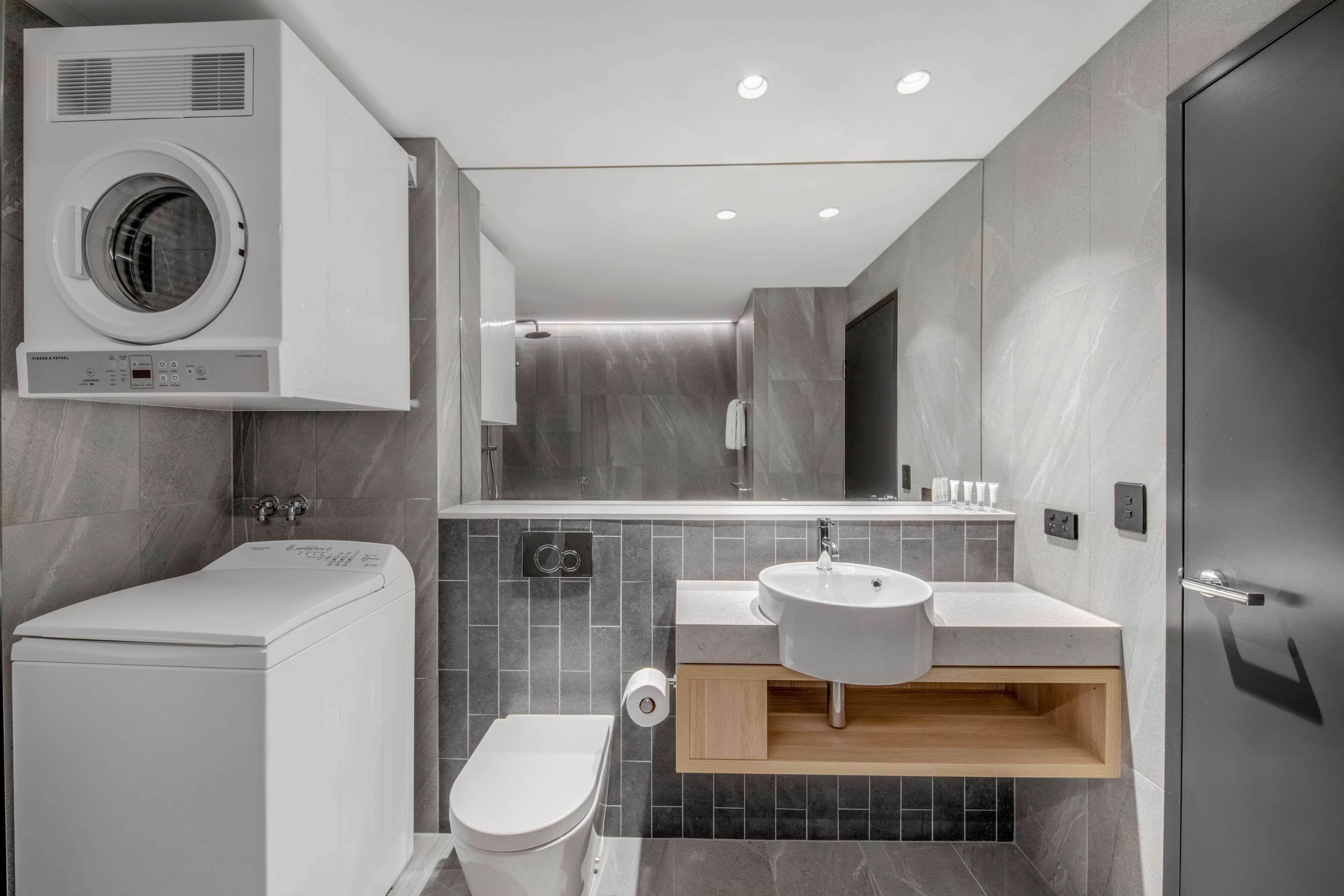 A modern bathroom with a built-in washer, toilet, sink, and mirror.