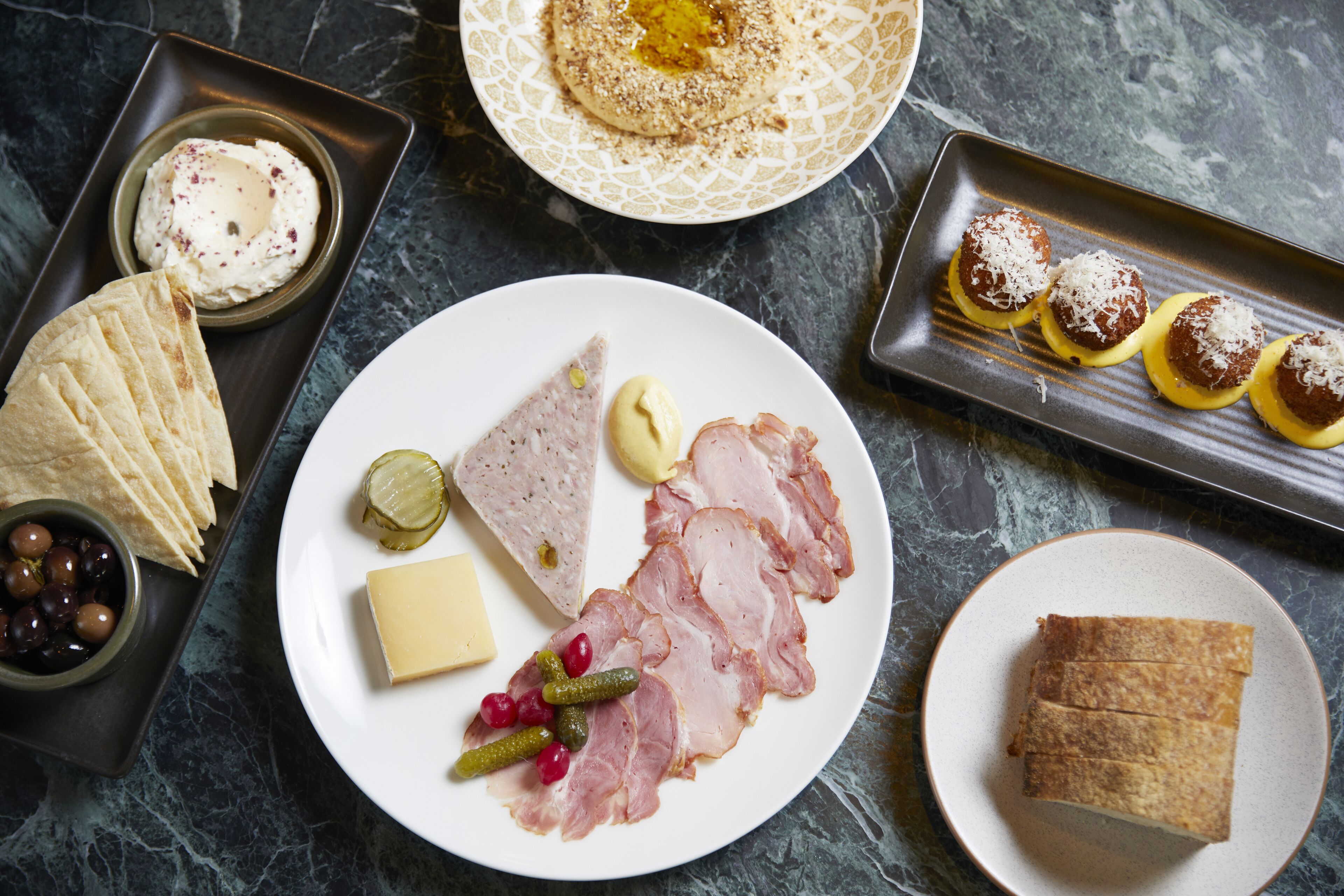 Variedad de alimentos como queso, jamón y pan sobre una mesa de mármol.