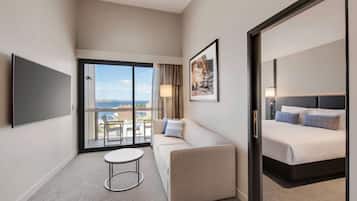 Quarto de hotel com sofá, cama, televisão, mesa pequena e varanda com vista.