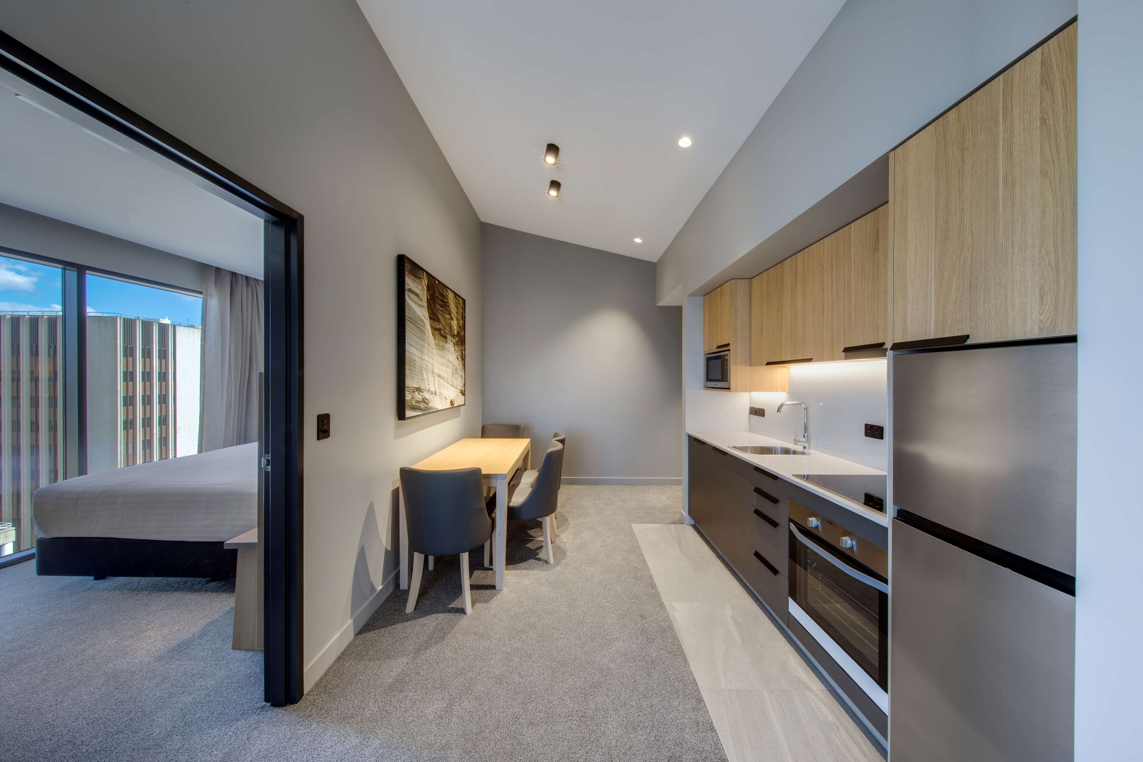 A modern kitchen with built-in appliances, a dining area with a table and chairs, and a large window offering a view of the cityscape.