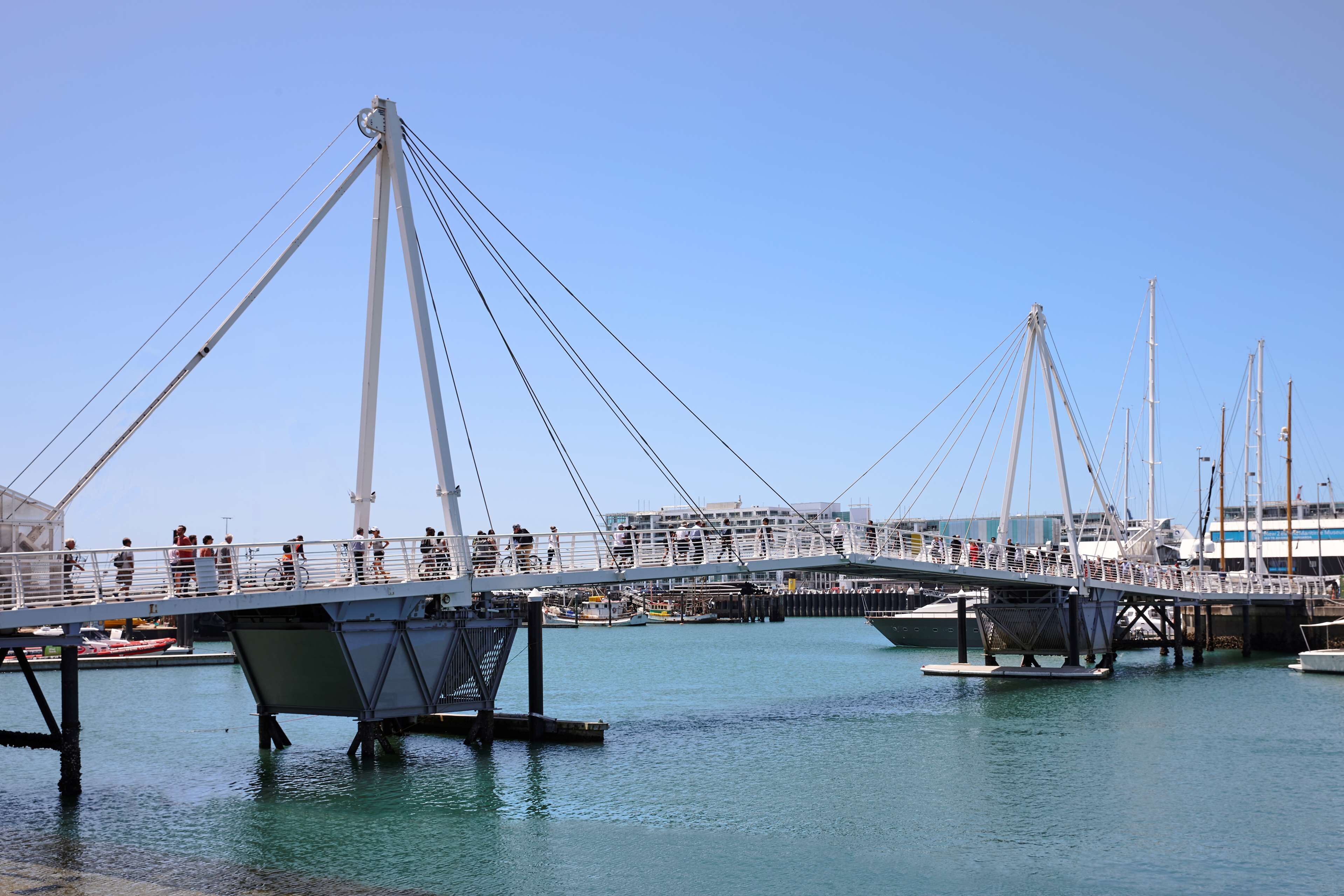 Eine Fußgängerbrücke über einem Gewässer, in dessen Nähe Boote liegen.