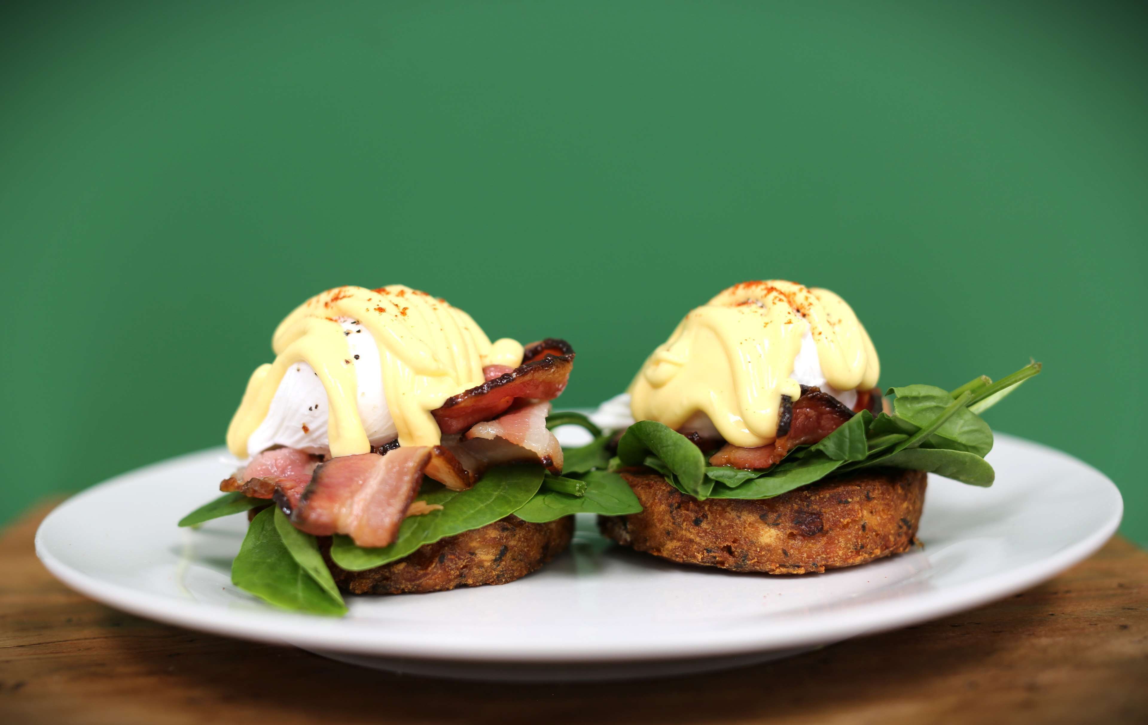Two breakfast sandwiches on a white plate with a green background.