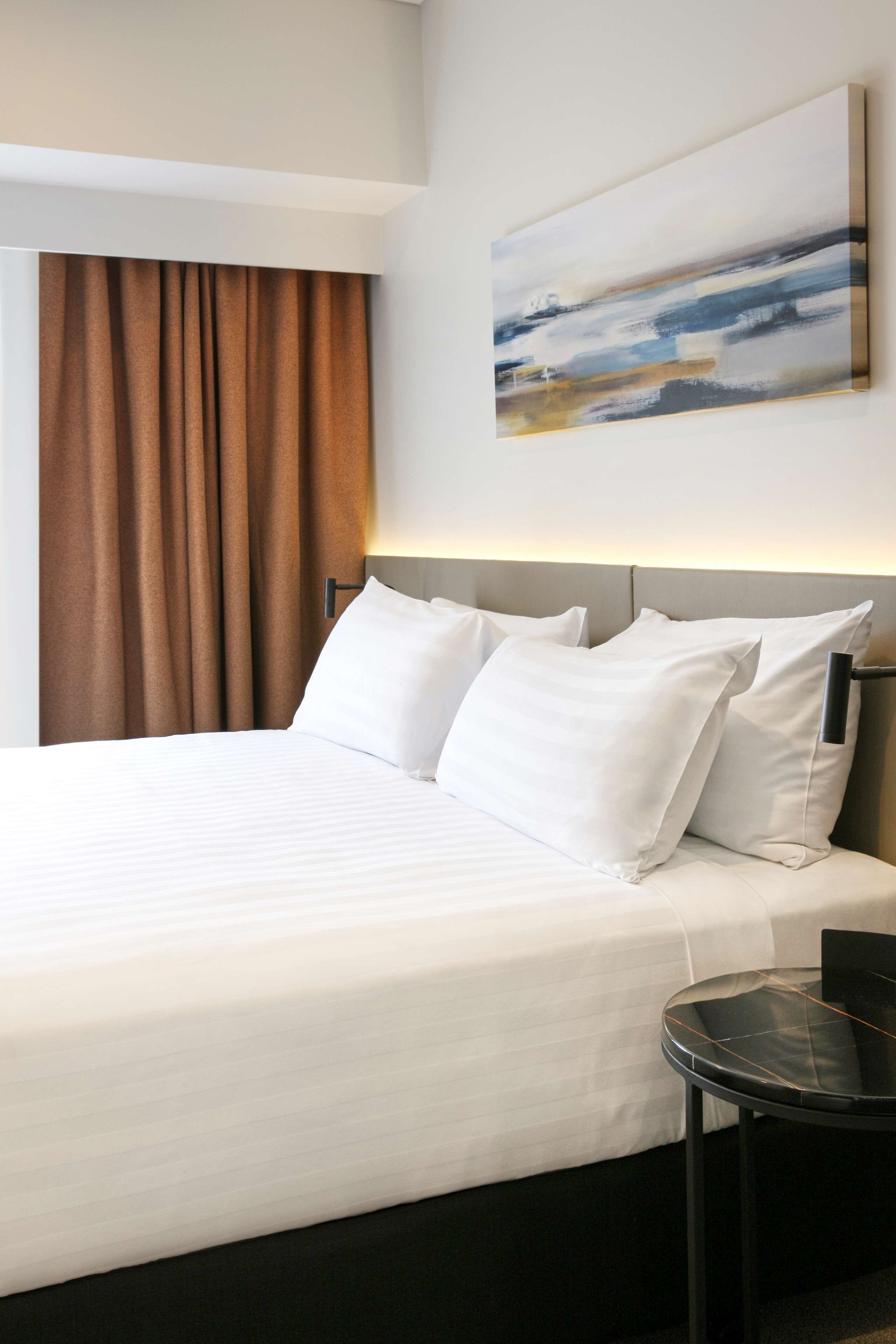 Een hotelkamer met een opgemaakt bed, een klein rond tafeltje en een schilderij aan de muur.
