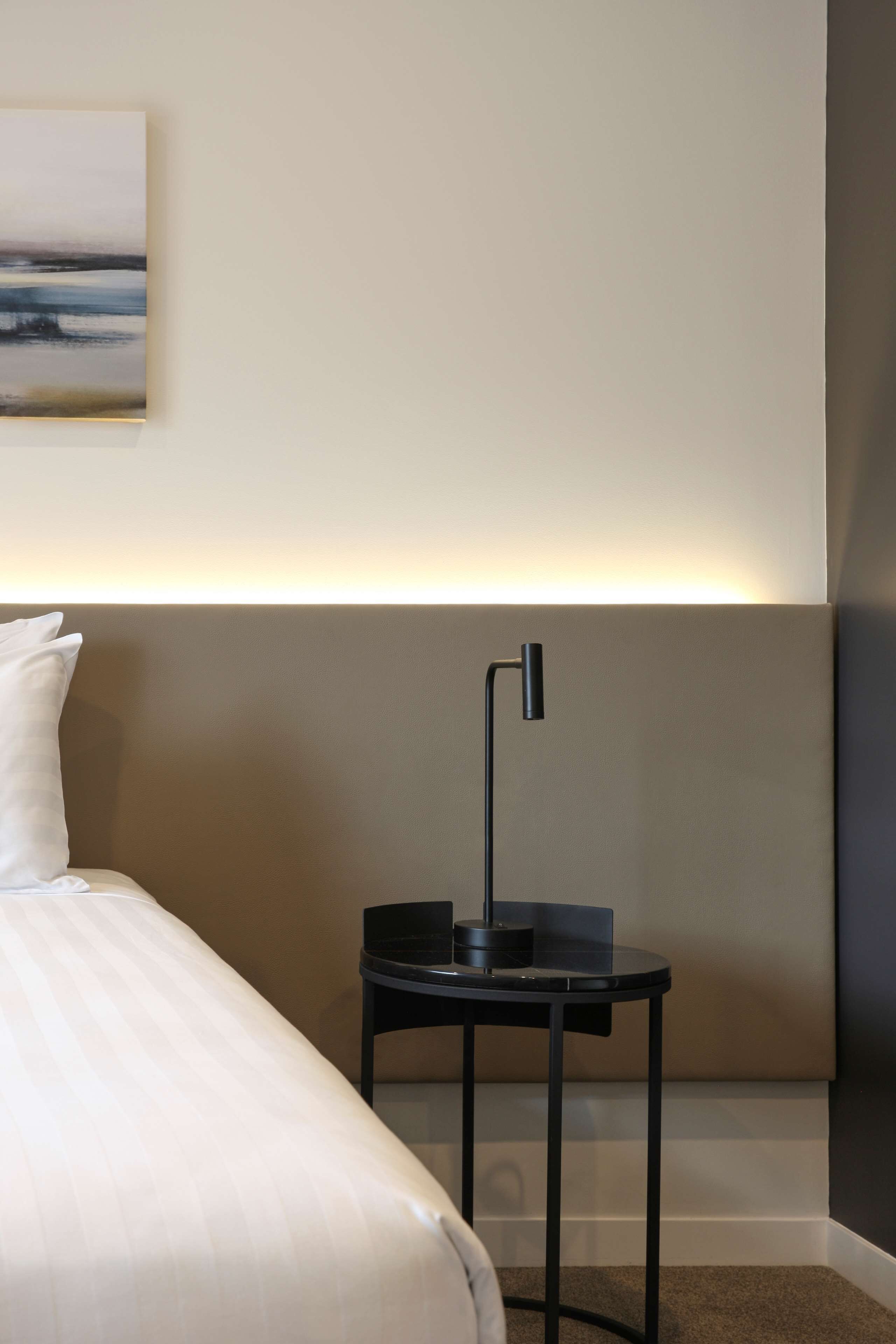 Una habitación de hotel con una cama, una mesita de noche, una lámpara y un cuadro en la pared.