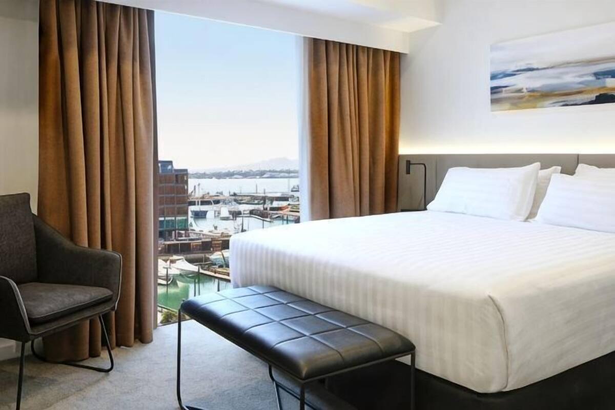 Hotellihuone, jossa on suuri sänky, penkki, tuoli ja näkymä venesatamaan.