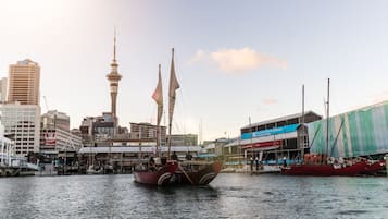 Een haven met een traditionele zeilboot, moderne gebouwen en een opvallende toren op de achtergrond.