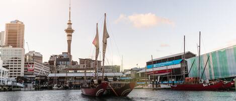 A harbor with a traditional sailing boat, modern buildings, and a prominent tower in the background.