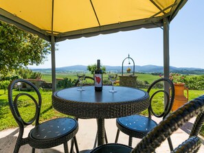 Ein runder Tisch mit Stühlen unter einer gelben Markise, mit Blick auf eine schöne Landschaft.
