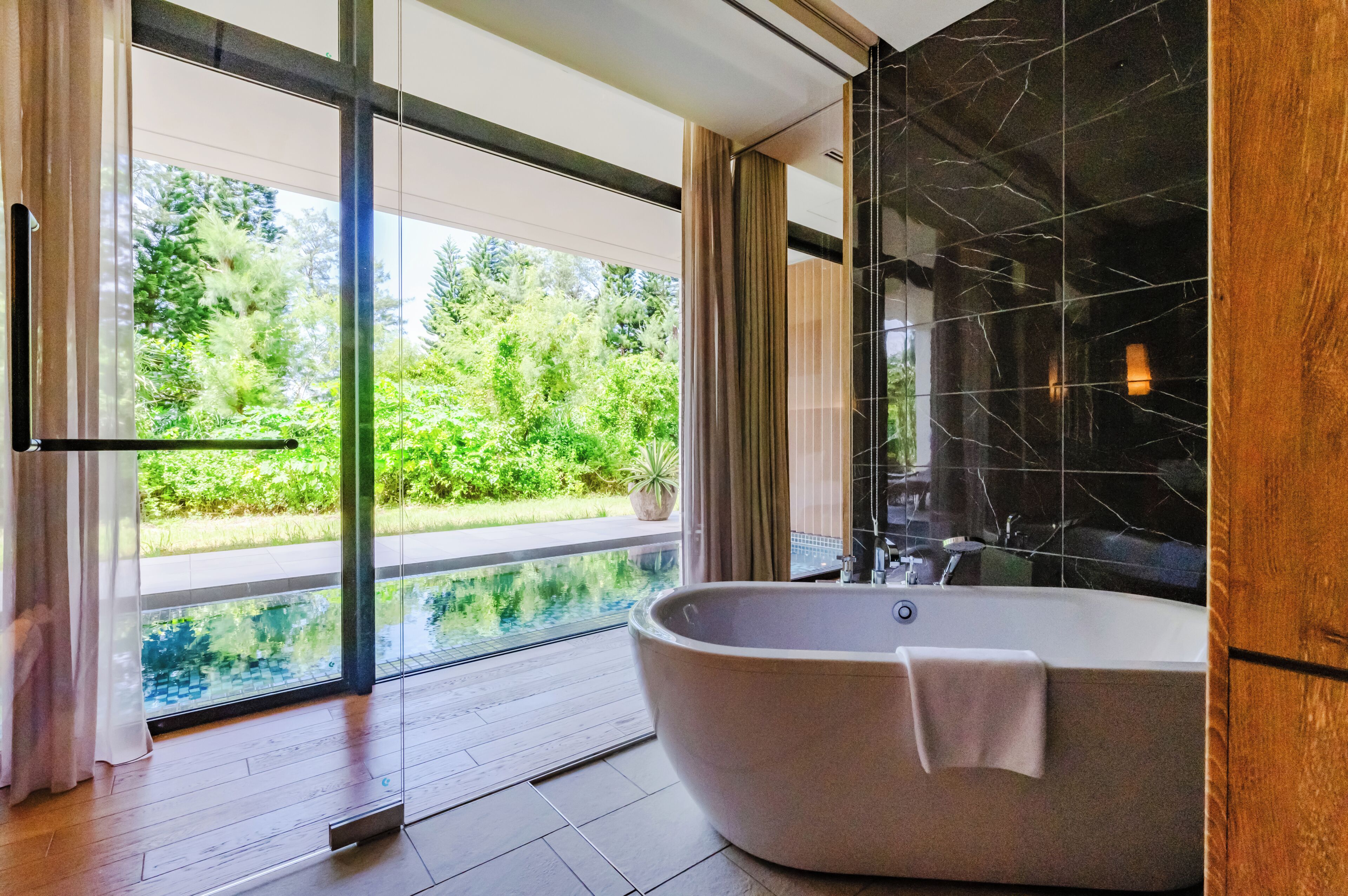 Un baño moderno con una bañera independiente, ducha con cerramiento de vidrio y vistas a un jardín exuberante.
