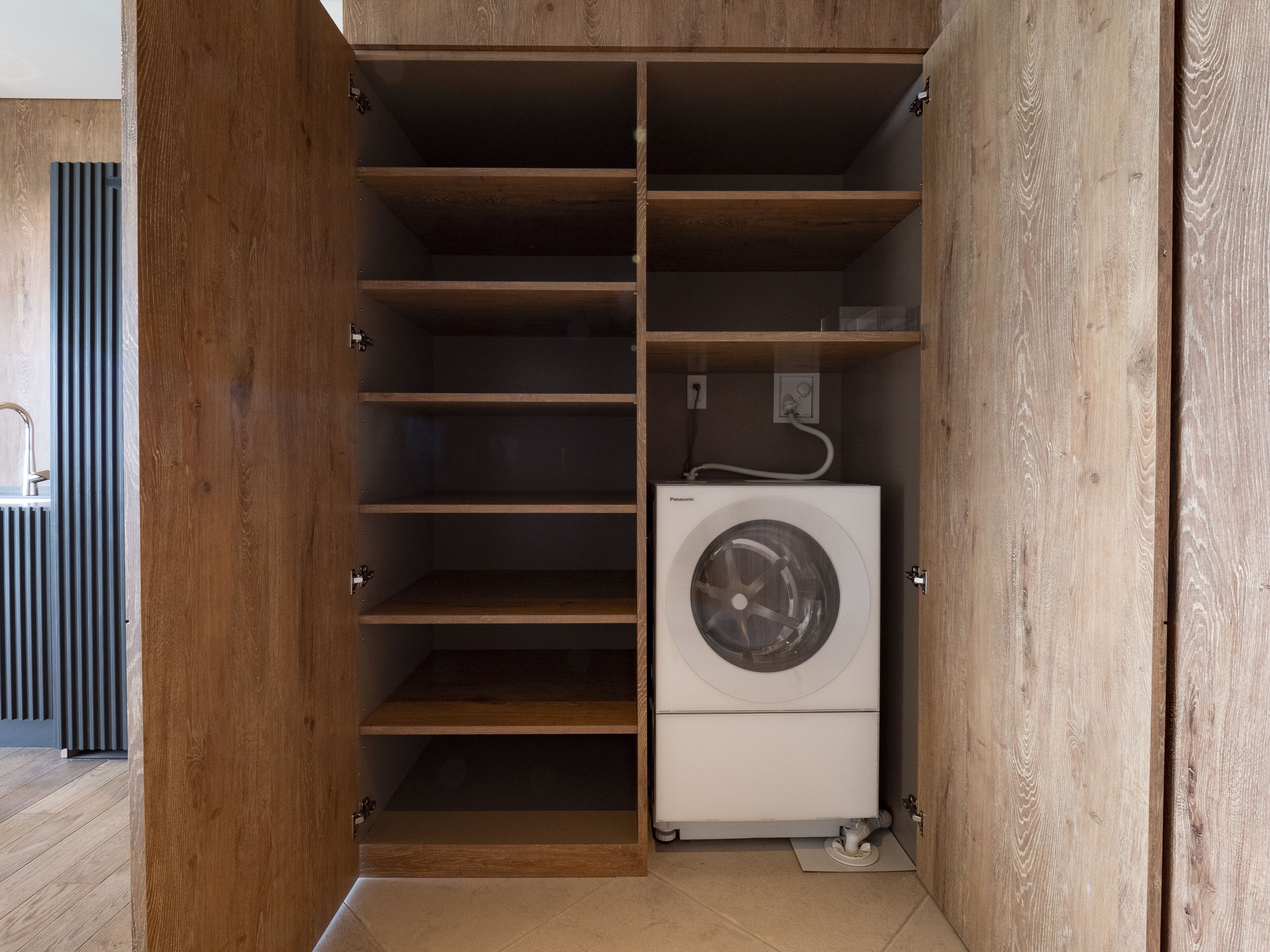 A compact, wooden-framed walk-in closet with multiple shelves and a built-in washing machine.