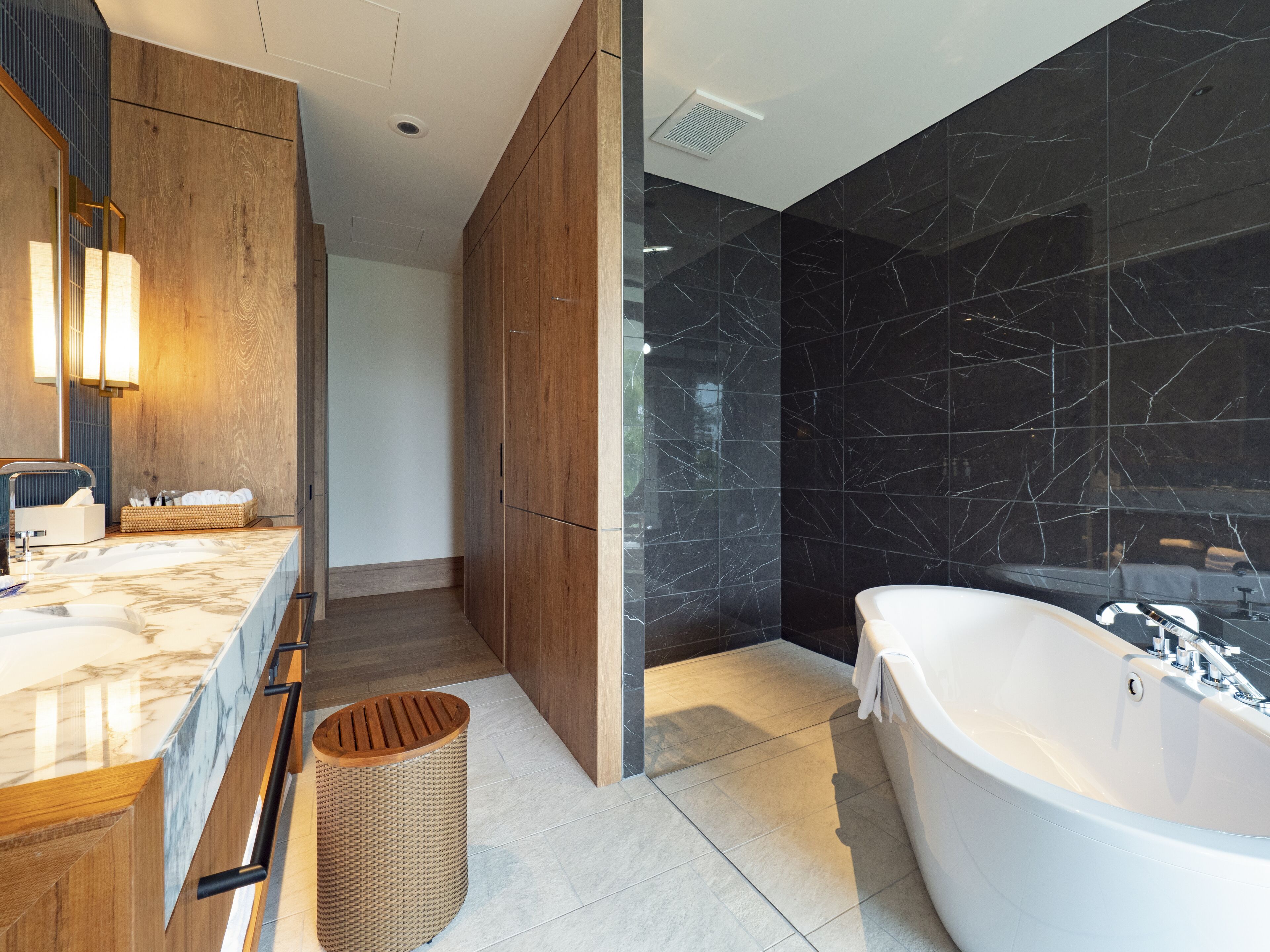 A modern bathroom with a marble vanity, a freestanding bathtub, and dark marble walls.
