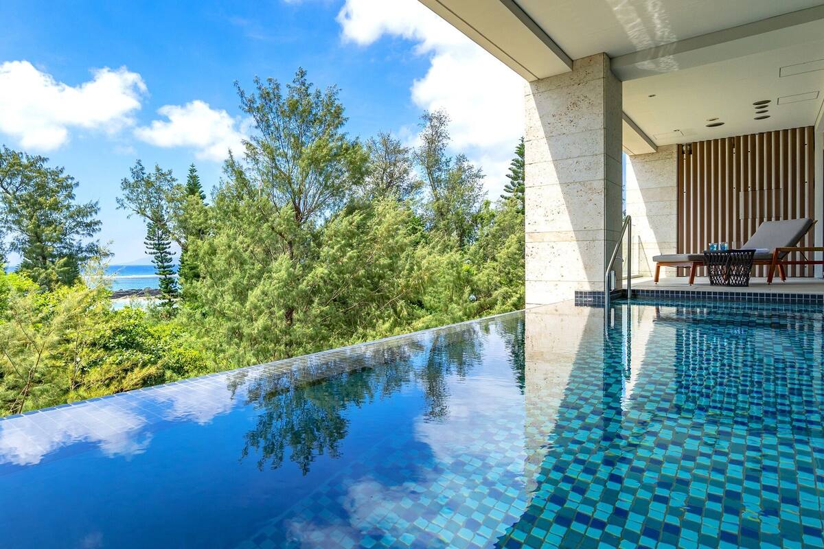 A modern infinity pool with a clear view of the ocean and lush greenery.