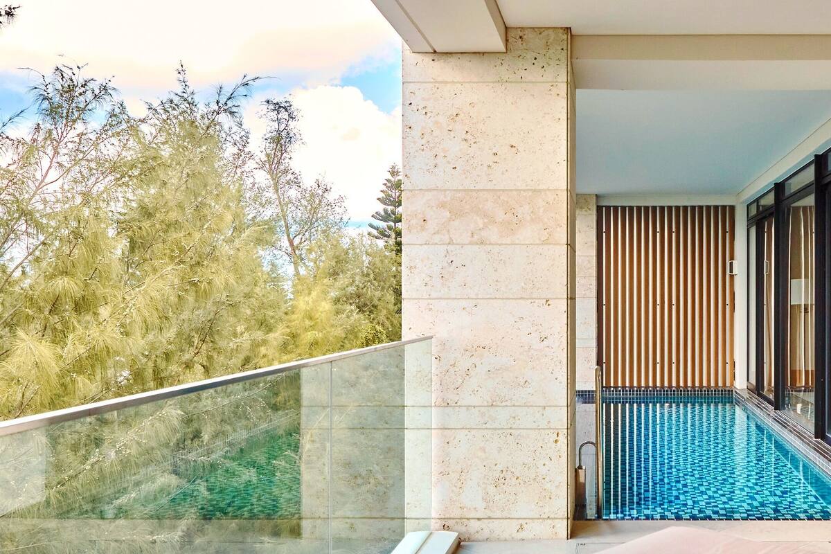 A balcony with a glass railing, a pool, and a view of trees.