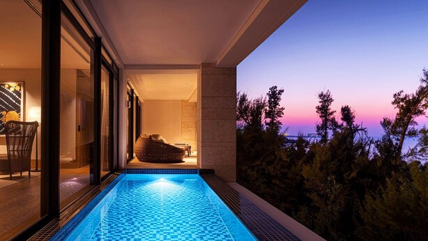 A modern indoor swimming pool with a view of trees and a sunset. - UMITO OKINAWA ONNASON (Onna)
