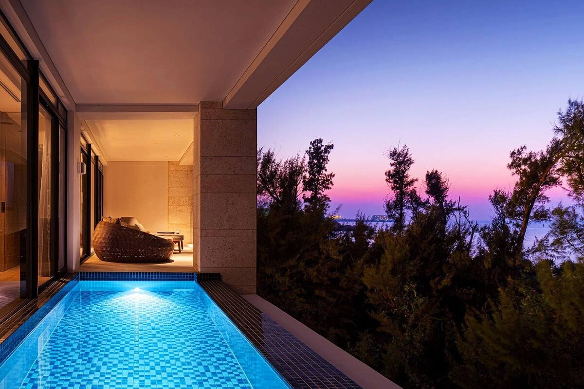 A modern indoor swimming pool with a view of trees and a sunset.