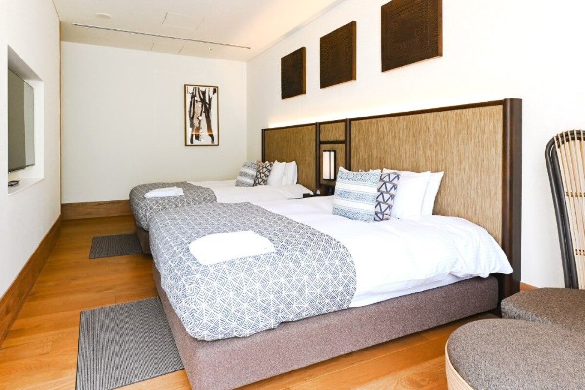 A hotel room with two beds, a large window, and a wall-mounted artwork.