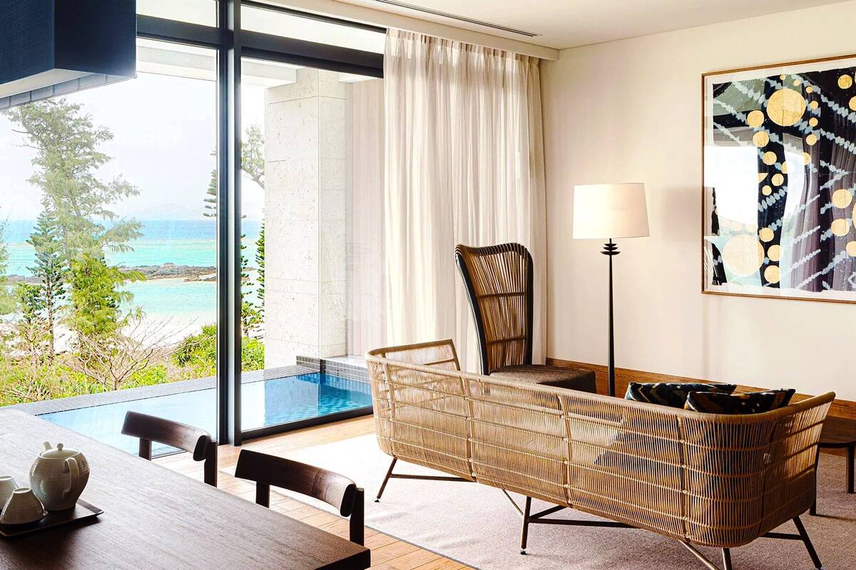 A modern room with a wooden dining table, wicker furniture, a floor lamp, and a large painting.