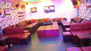 A lounge area with red cushioned seating, a flat-screen TV mounted on the wall, and a patterned wall design. - Tuscany Suites (Port Harcourt)