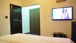 A hotel room with a bed, a television mounted on the wall, a door, and a small table with a remote control. - Tuscany Suites (Port Harcourt)