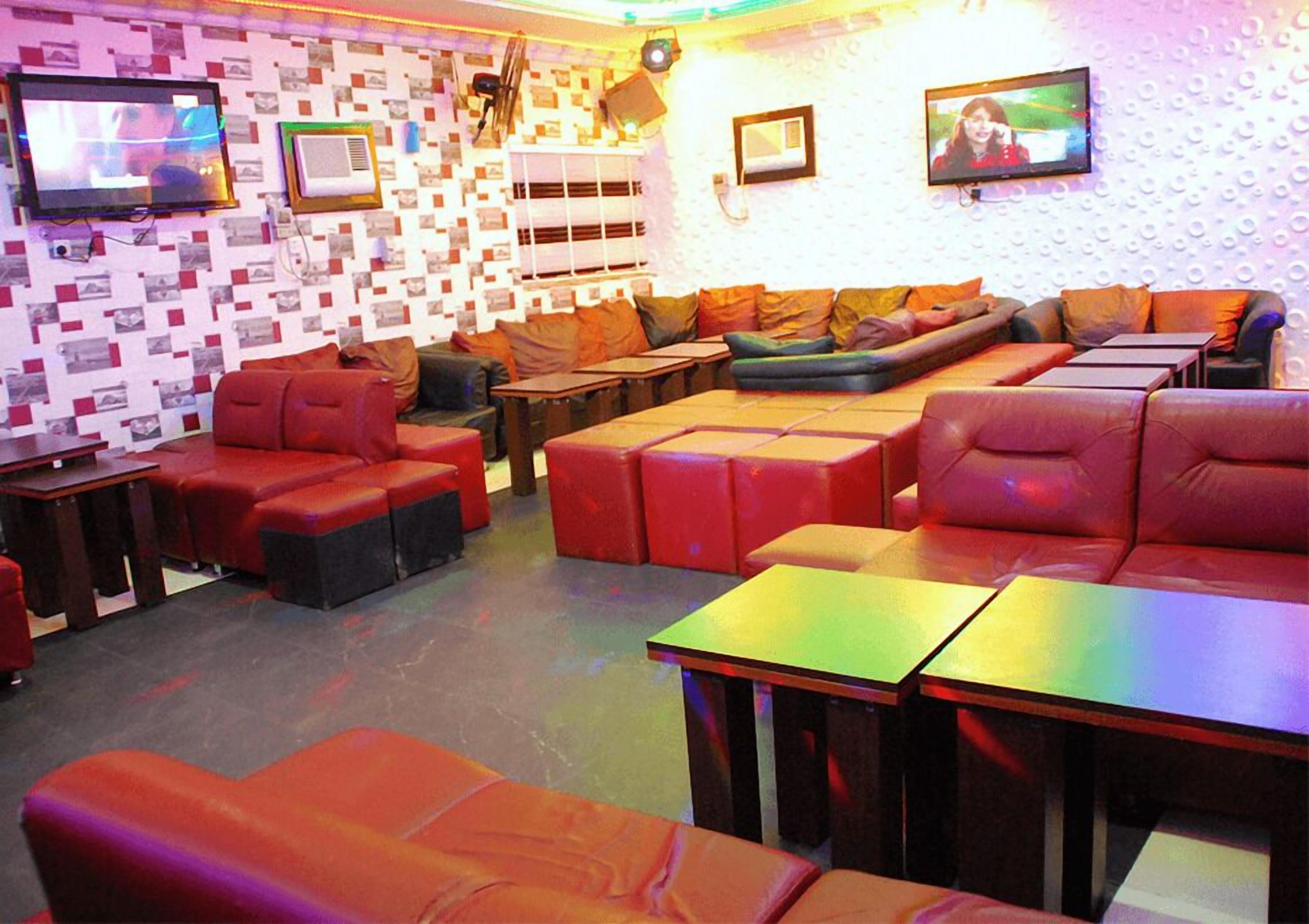 Un espace détente avec des fauteuils et des canapés en cuir rouge et noir, un mur orné de motifs et deux téléviseurs fixés au mur.