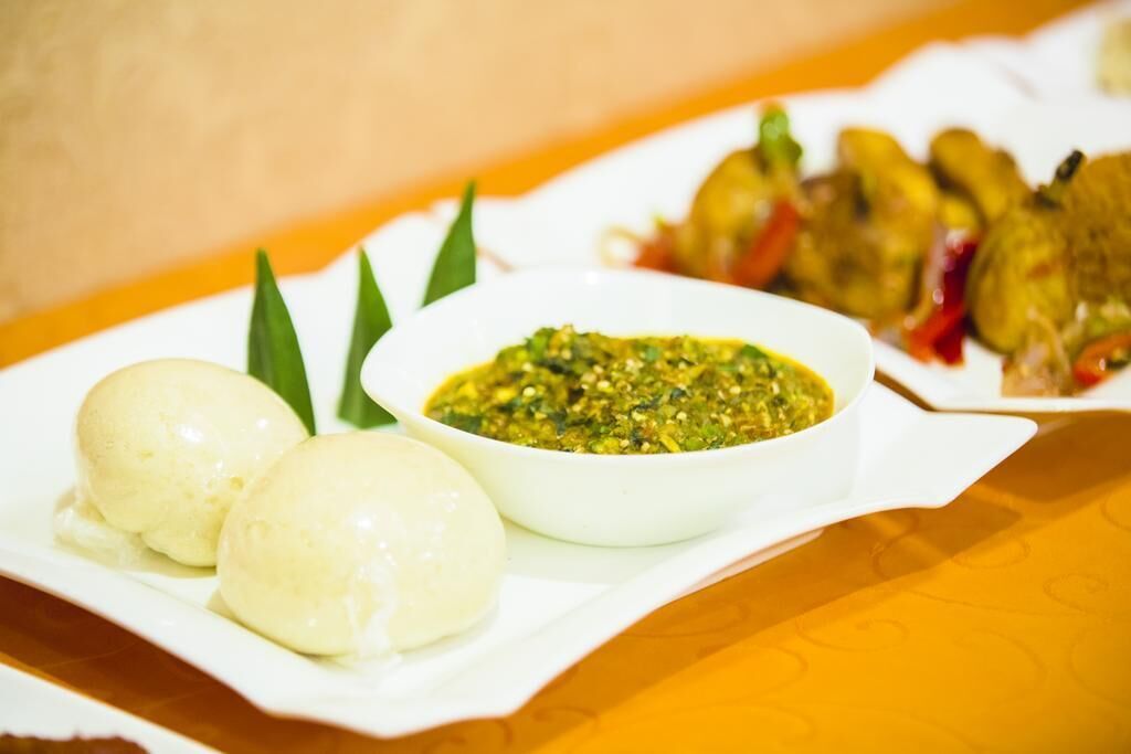 A plate with two white dumplings, a bowl of green sauce, and grilled vegetables.