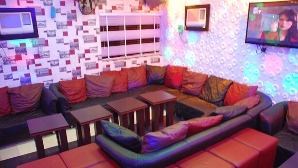 A modern lounge area with a sectional sofa, small tables, and a patterned wall. - Tuscany Suites (Port Harcourt)