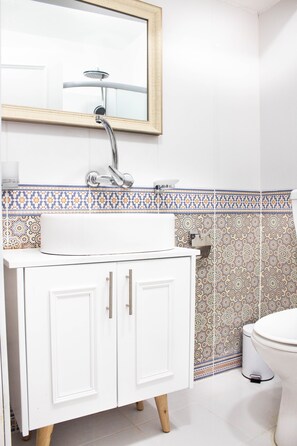 A bathroom with a white vanity, a shower, and patterned tiles.