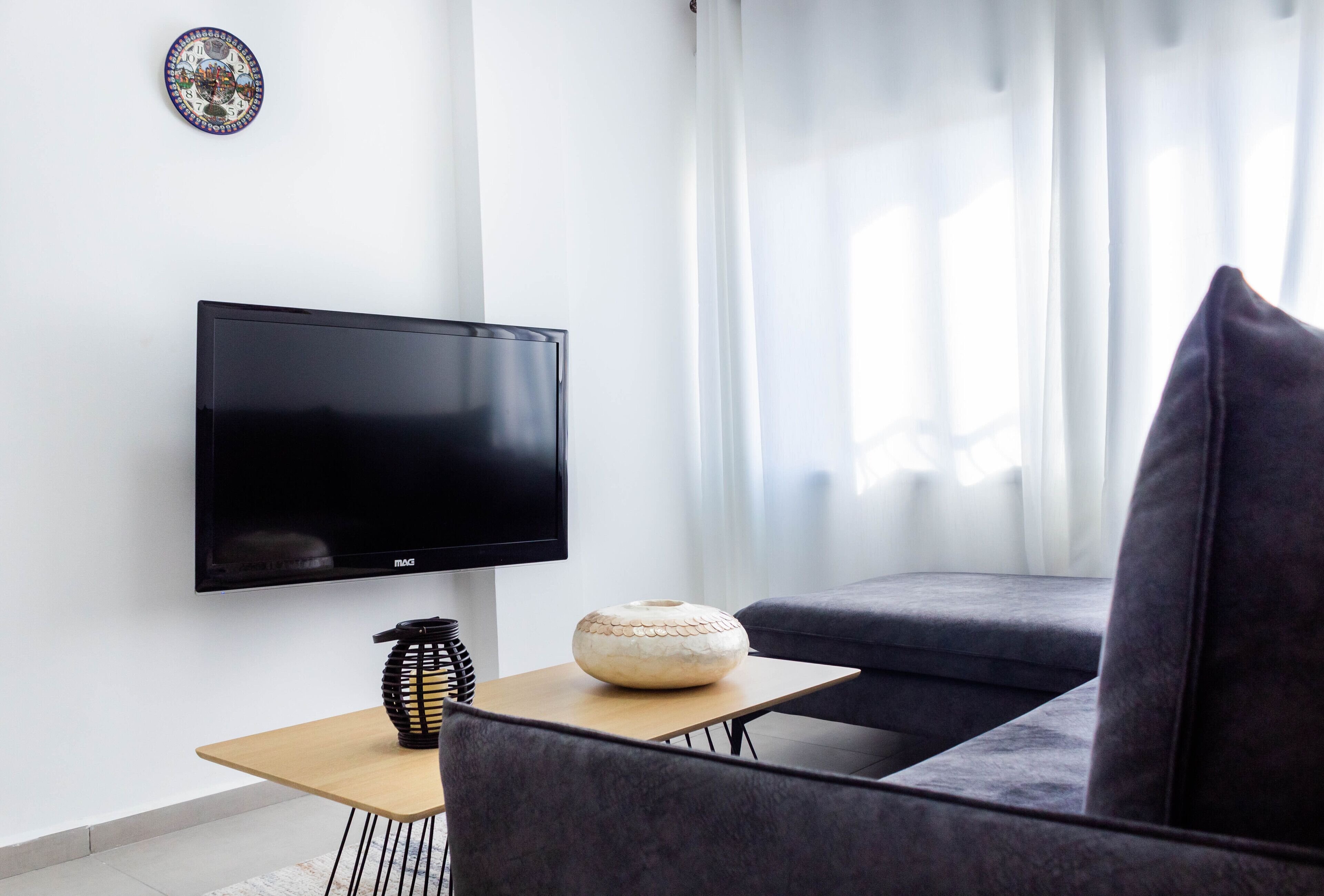 A modern living room with a flat-screen TV, a round decorative item on a small table, and a dark sofa.