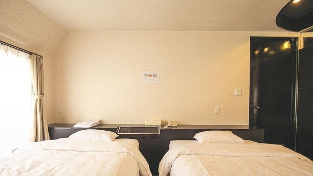 A hotel room with two single beds, a bedside table with a lamp, a small table with a phone and a book, and a wall-mounted sign. - Osaka Grand Hotel (Higashi-osaka)