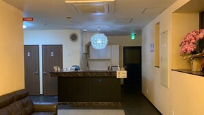 A hotel lobby with a reception desk, a clock, a decorative light fixture, a sofa, and a wall-mounted flower arrangement. - Osaka Grand Hotel (Higashi-osaka)
