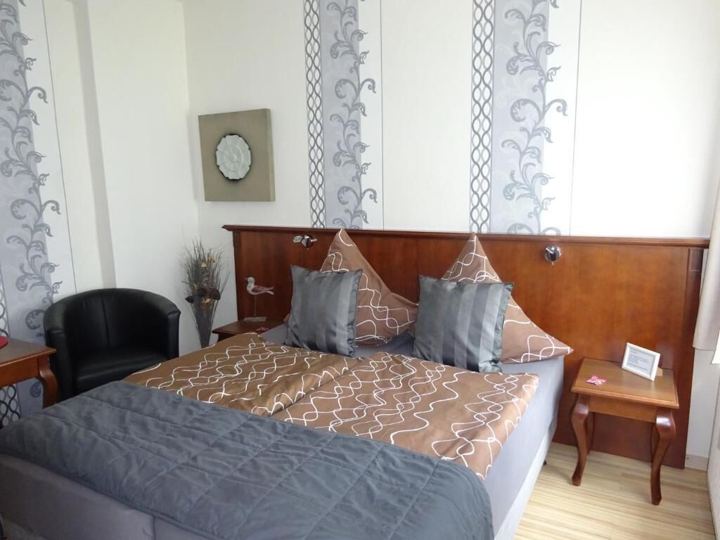 Um quarto bem arrumado com uma cama grande, cabeceira de madeira, uma mesinha e uma cadeira.