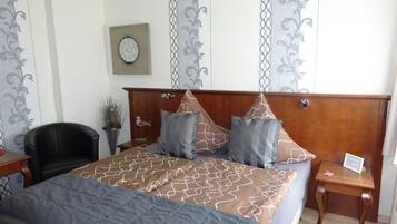 Um quarto bem arrumado com uma cama grande, cabeceira de madeira, uma mesinha e uma cadeira.