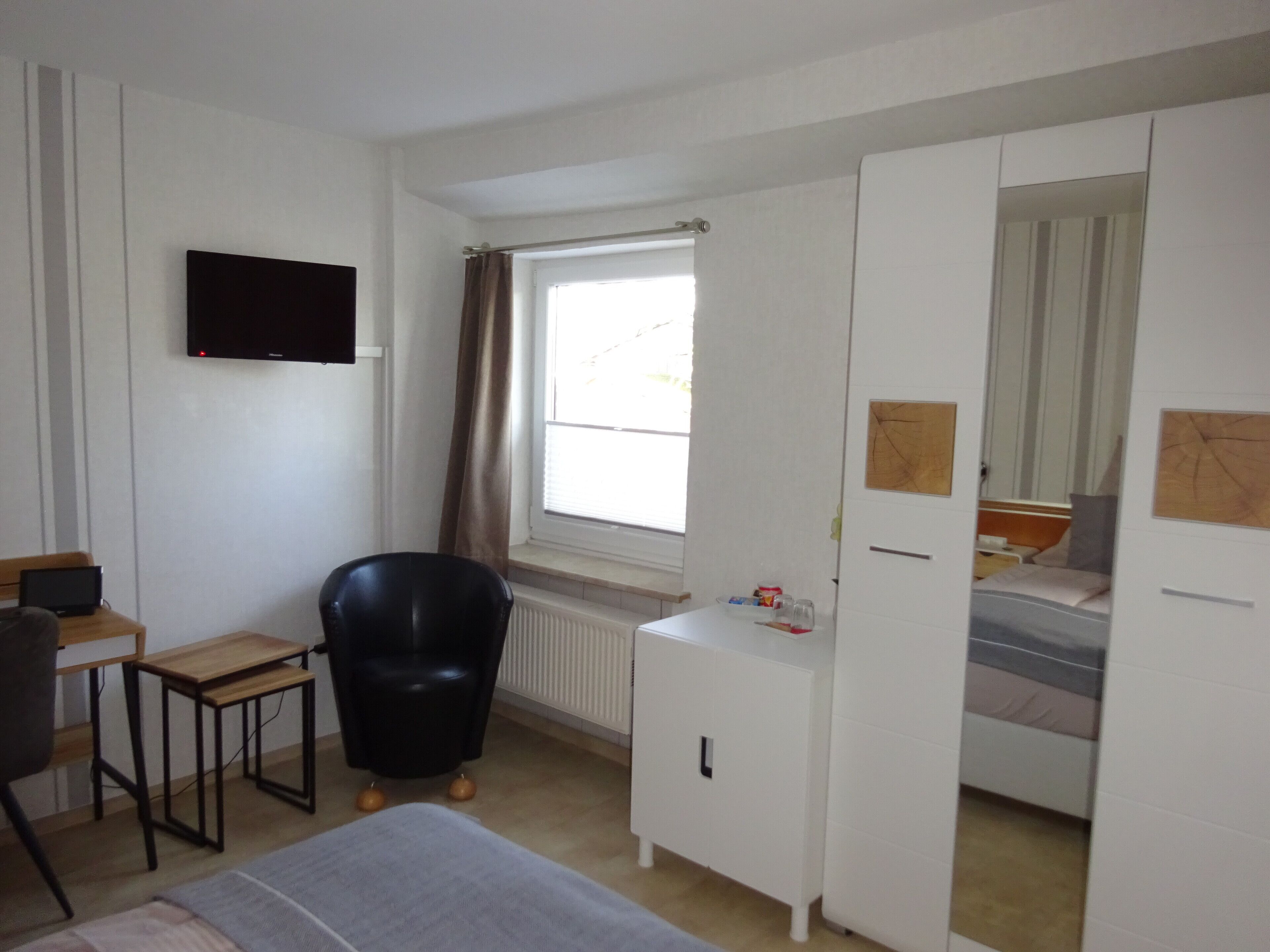 A bedroom with a bed, a desk, a chair, a wardrobe, a television, and a window with curtains.
