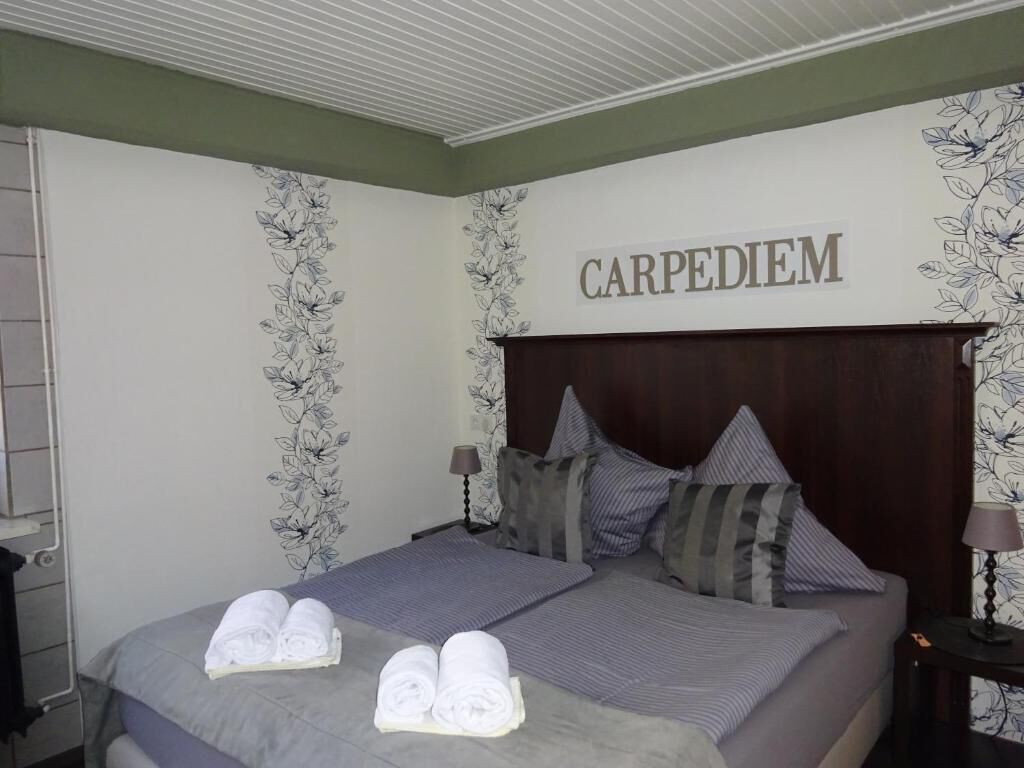 Une chambre d’hôtel avec un lit, deux oreillers, une tête de lit et un mur orné d’un motif floral et du mot «CARPE DIEM».