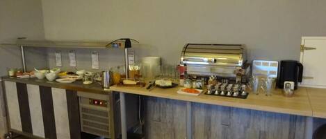 A self-service breakfast bar with various food items and beverages, a coffee machine, and a microwave.