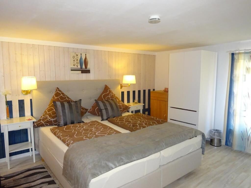 Une chambre à coucher avec un lit, des tables de chevet, des lampes, une armoire et une fenêtre avec des rideaux.