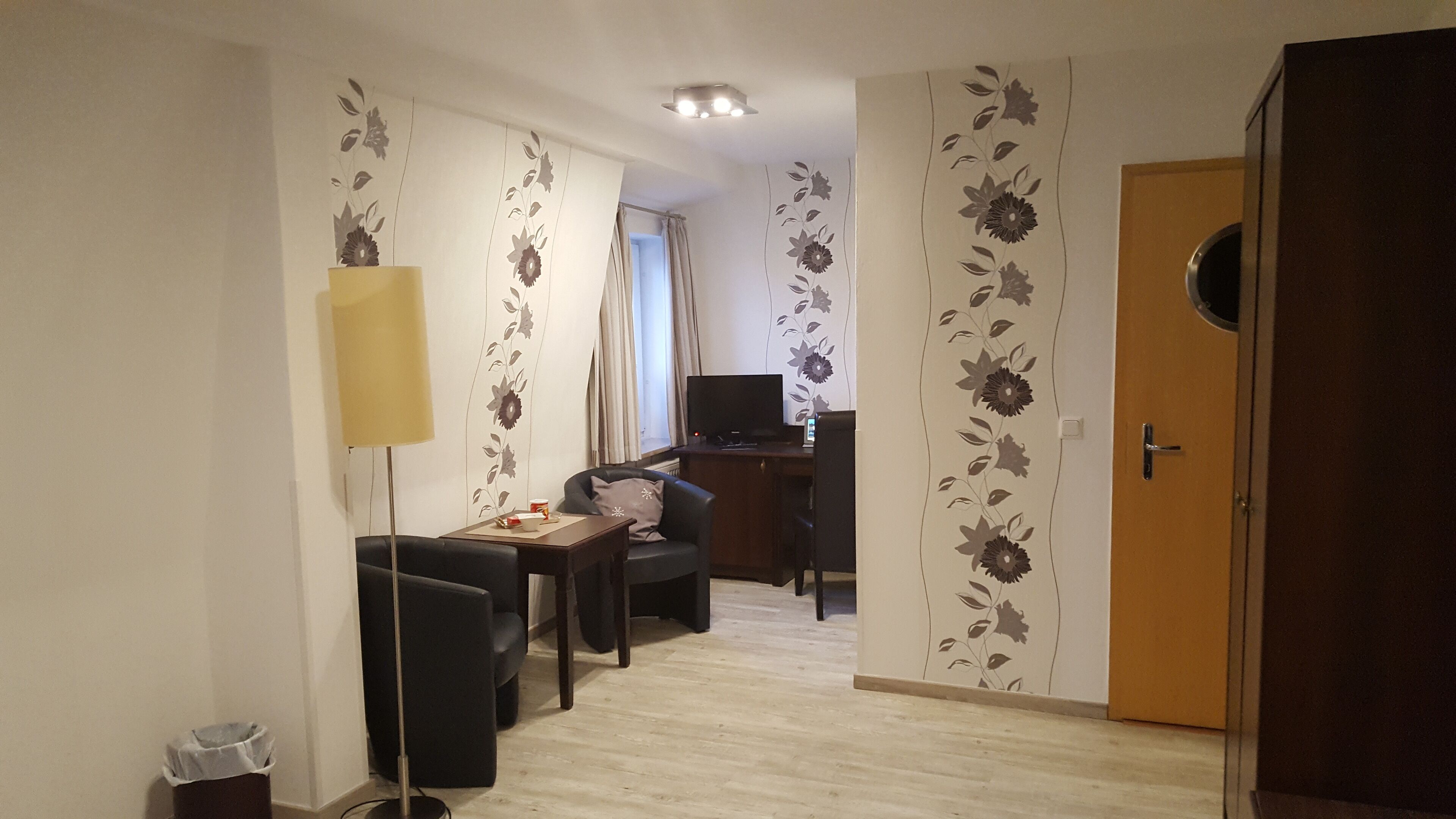 Una habitació amb escriptori, cadira, televisió, làmpada i porta.